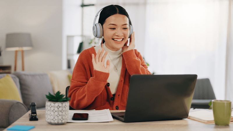 Young woman waving at computer screen in home office